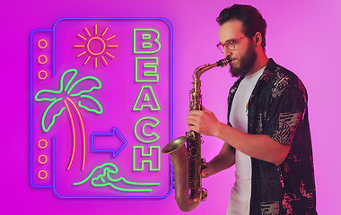 Image showing Young jazz musician playing the saxophone in neon light with neon sign