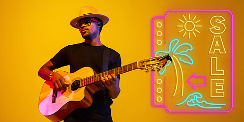 Image showing Young musician playing guitar in neon light on gradient background, inspired, artwork