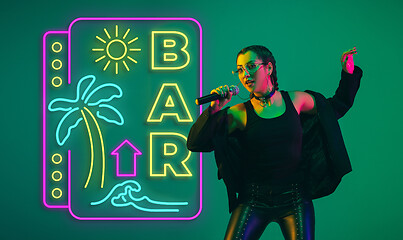 Image showing Caucasian female singer portrait isolated on gradient studio background in neon light with neon sign