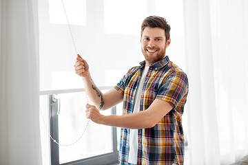 Image showing man opening roller blind on window at home