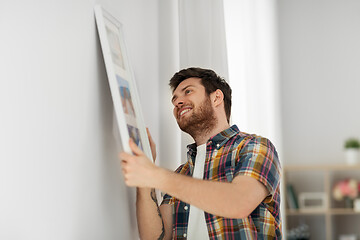 Image showing man hanging picture in frame to wall at home