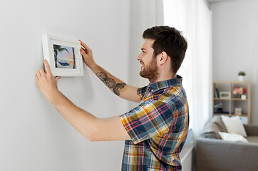 Image showing man hanging picture in frame to wall at home