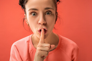 Image showing The young woman whispering a secret behind her hand over coral background