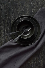 Image showing Kitchen table served with black utensils ceramic plates, spoon, fork and textile napkin.