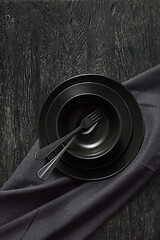 Image showing Served kitchen table with black cookware ceramic plates, fork, spoon and textile napkin.