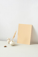 Image showing Ceramic vases with dry natural twig and vertical paper sheet on a light grey background.