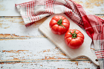 Image showing Top view of a white cutting board with a fresh juicy tomatoes on a wooden table