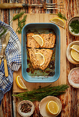 Image showing Roasted salmon in heat proof dish. With aromatic dill, lemon, salt and pepper on sides.