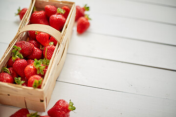 Image showing Wooden container with fresh red strawberries. Placed on white table.