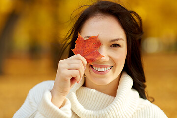 Image showing happy young woman with maple leaf in autumn park