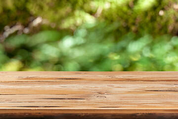 Image showing Aged wooden table for montage or display products on a green leaves blurred background.