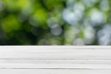 Image showing Old wooden light grey table for display or montage your products on a green leaves blurred background.