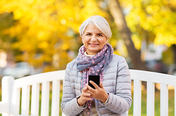 Image showing happy senior woman with smartphone at autumn park