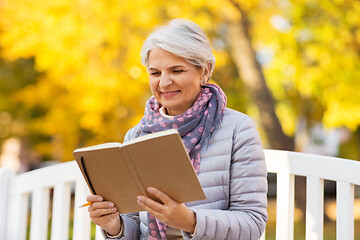 Image showing happy senior woman reading diary at autumn park