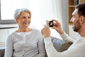 Image showing adult son photographing senior mother at home