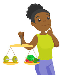 Image showing African-american woman weighing food and dumbbell.