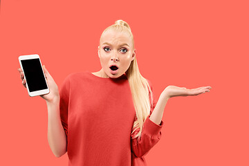 Image showing Portrait of a confident casual girl showing blank screen mobile phone isolated over coral background