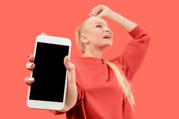 Image showing Portrait of a confident casual girl showing blank screen mobile phone isolated over coral background