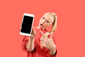 Image showing Portrait of a confident casual girl showing blank screen mobile phone isolated over coral background