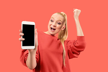 Image showing Portrait of a confident casual girl showing blank screen mobile phone isolated over coral background