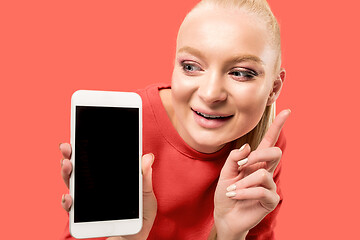 Image showing Portrait of a confident casual girl showing blank screen mobile phone isolated over coral background