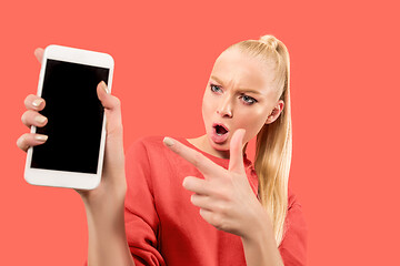 Image showing Portrait of a confident casual girl showing blank screen mobile phone isolated over coral background