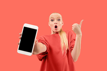 Image showing Portrait of a confident casual girl showing blank screen mobile phone isolated over coral background