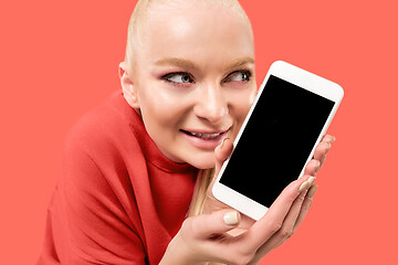 Image showing Portrait of a confident casual girl showing blank screen mobile phone isolated over coral background