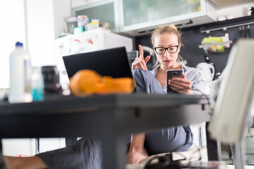 Image showing Stay at home and social distancing. Woman in her casual home clothing working remotly from kitchen dining table. Video chatting using social media with friend, family, business clients or partners