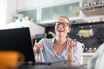 Image showing Stay at home and social distancing. Woman in her casual home clothing working remotly from kitchen dining table. Video chatting using social media with friend, family, business clients or partners