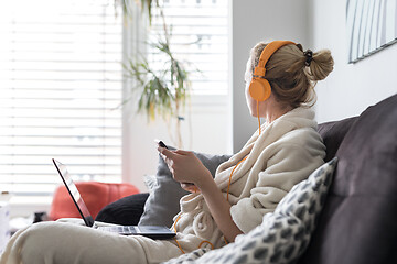 Image showing Social distancing. Stay at home. Woman in bathrobe being comfortable at her home sofa, using social media apps on phone for video chatting and stying connected with her loved ones.