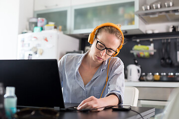 Image showing Female freelancer in her casual home clothing working remotly from her dining table in the morning. Home kitchen in the background.