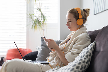 Image showing Social distancing. Stay at home. Woman in bathrobe being comfortable at her home sofa, using social media apps on phone for video chatting and stying connected with her loved ones.