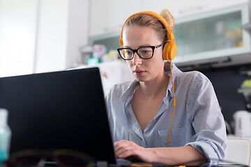 Image showing Female freelancer in her casual home clothing working remotly from her dining table in the morning. Home kitchen in the background.