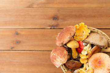 Image showing basket of different edible mushrooms on wood