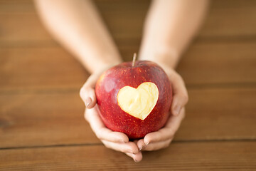 Image showing close up of hands holding apple with carved heart