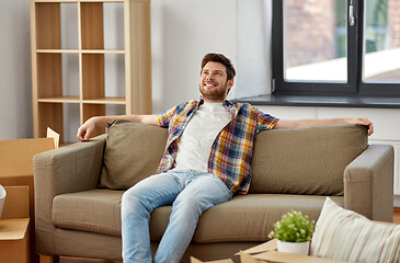 Image showing happy man with boxes sitting on sofa at new home