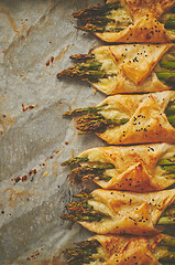 Image showing Green asparagus baked with cheese, wrapped in puff pastry. Placed on baking paper with copy space