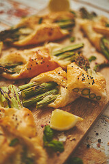 Image showing Baked green asparagus wrapped in puff pastry. Served on wooden board. With selective focus