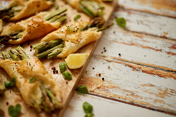 Image showing Baked green asparagus wrapped in puff pastry. Served on wooden board. With copy space