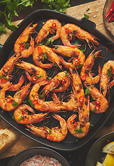 Image showing Roasted tiger prawns on iron grilling pan with fresh persley, lemon, chilli and bread