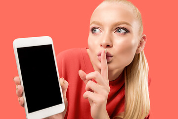 Image showing Portrait of a confident casual girl showing blank screen mobile phone isolated over coral background