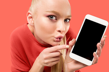 Image showing Portrait of a confident casual girl showing blank screen mobile phone isolated over coral background