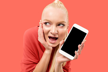 Image showing Portrait of a confident casual girl showing blank screen mobile phone isolated over coral background