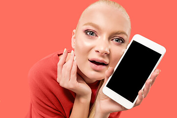 Image showing Portrait of a confident casual girl showing blank screen mobile phone isolated over coral background