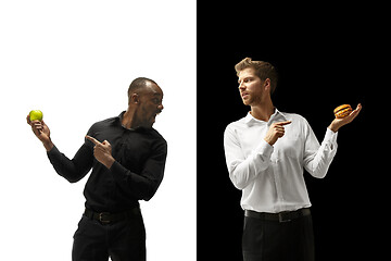 Image showing Men eating a hamburger and fruits on a black and white background