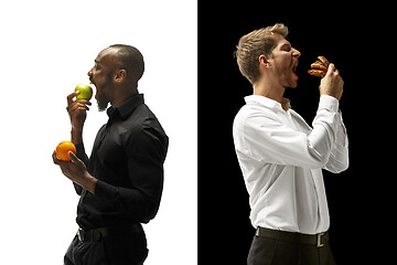 Image showing Men eating a hamburger and fruits on a black and white background