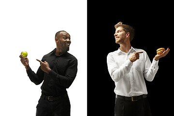 Image showing Men eating a hamburger and fruits on a black and white background