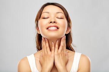 Image showing happy smiling young asian woman touching her face