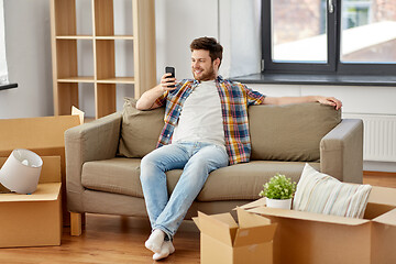 Image showing man with smartphone and boxes on sofa at new home